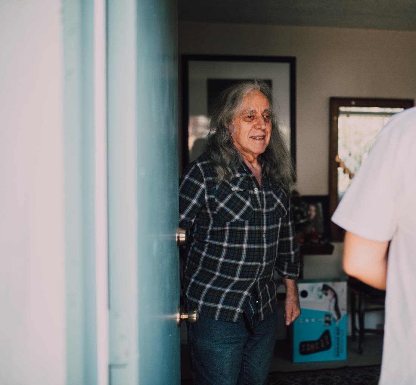 An older man welcoming his regular carer at the front door of his home