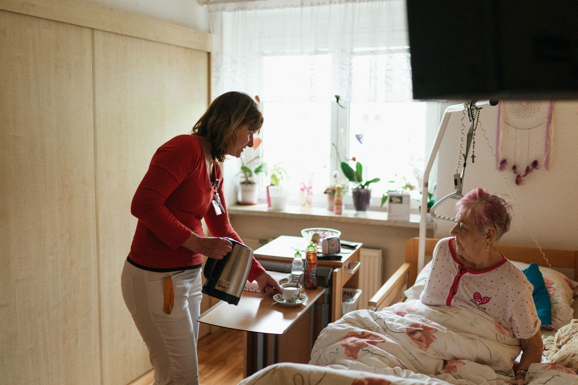A carer gently checking on an older woman resting at home in the evening