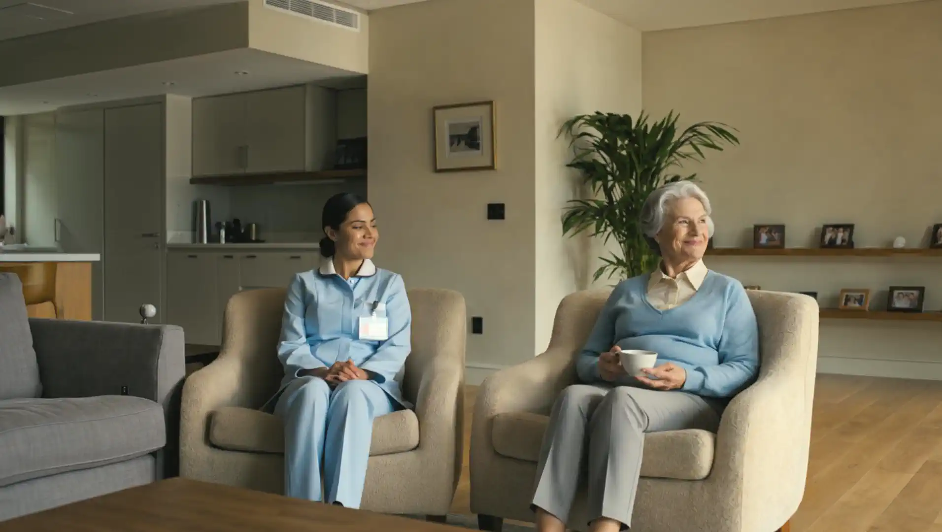 A carer in uniform sitting with an older woman in her front room while she has a cup of tea